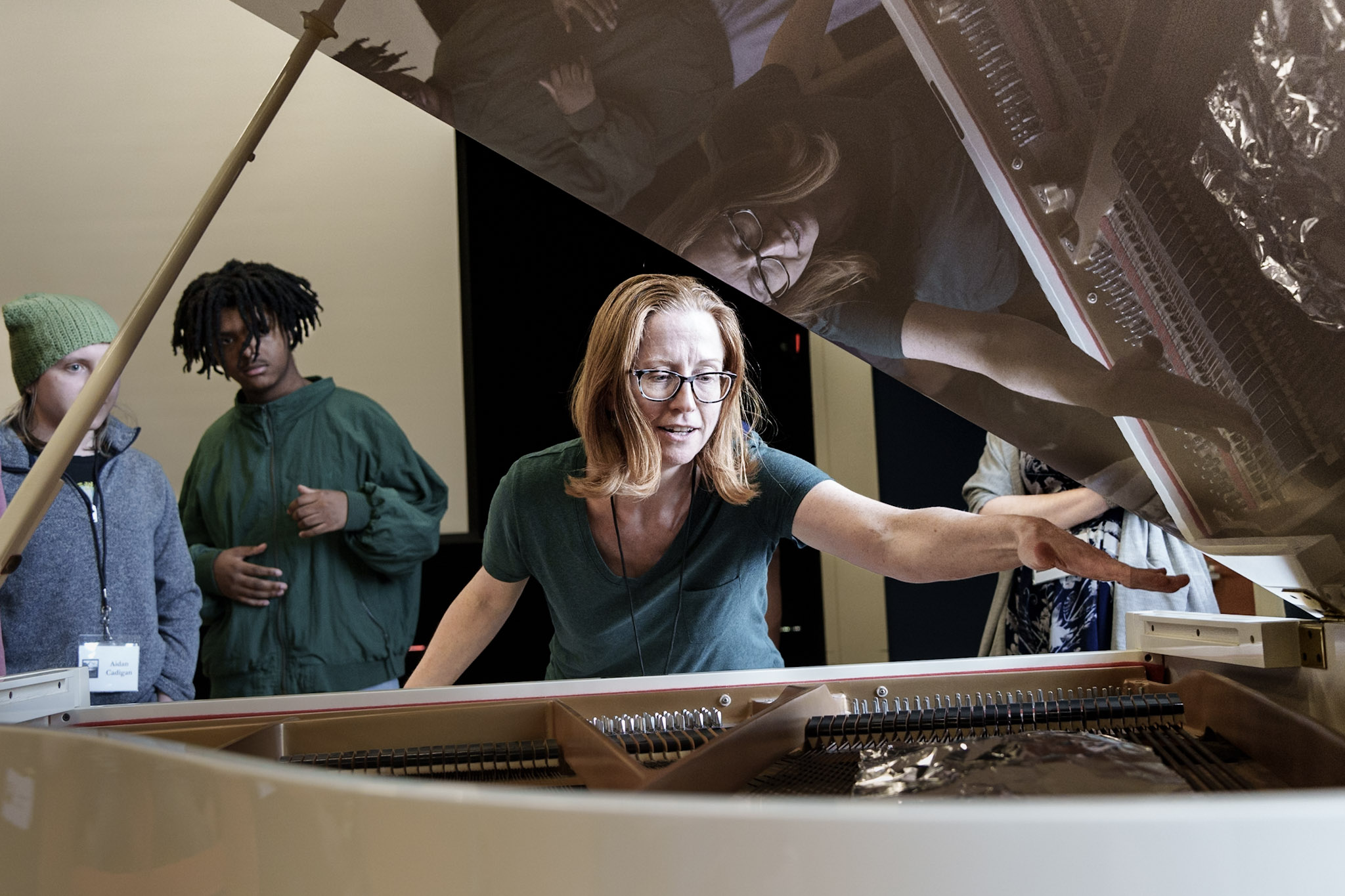 Renée leans over an open grand piano, gesturing at the strings